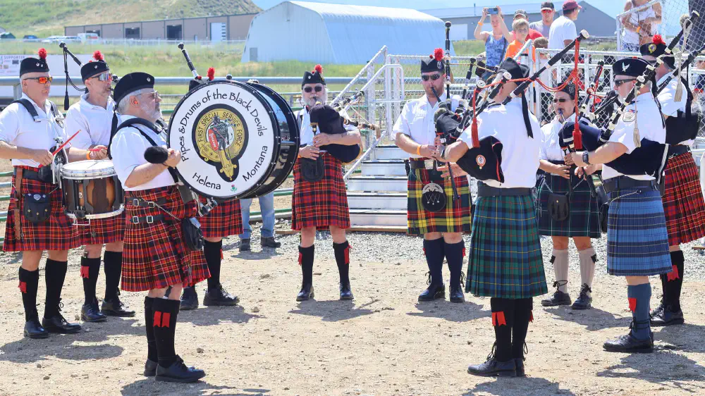 Pipers and drummers performing outdoors, with the Pipes and Drums of the Black Devils name on the bass drum
