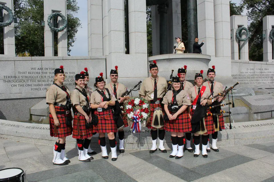 Band members gathered beside a wreath at a stone memorial.